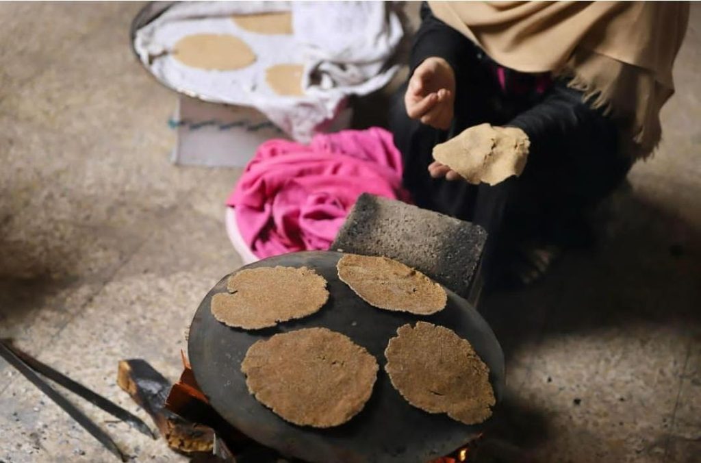 4 very thin flatbreads on a hot plate. A woman's hand holds another piece of flattened dough.