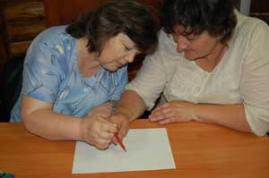 Une aide-enseignante et un enseignant du système classique dessinent ensemble avec un seul crayon. Le but de l'activité est de provoquer l'autoréflexion sur le travail d'équipe, montrer et suivre un exemple.