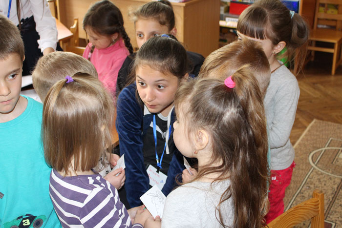 female student (young researcher) surrounded by kindergarten children. Student is listening to what a child is saying