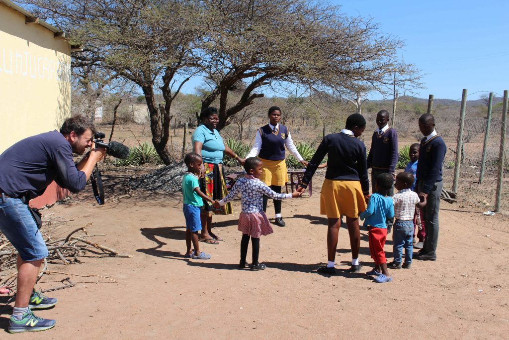 Cameraman filming a circle of older and younger children holding hands