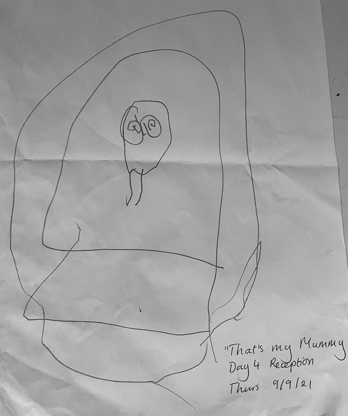 A child's line drawing on paper. There are words written by the side (we assume by an adult) "That's my Mummy. Day 4 Reception. Thurs 9/9/21)". The image has a rough circle on the middle which may be a head, and 2 circles inside that which may be eyes. These are surrounded by a rough oval shape.