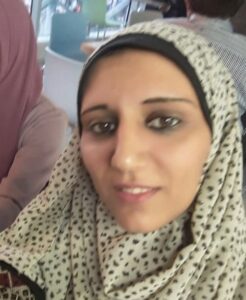 A headshot of Alaa Qwaider smiling at the camera wearing a black and white spotted headscarf. 