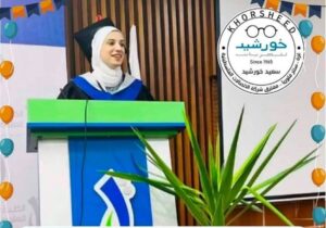 Yasmine Khorshid stands on a podium, smiling and addressing an audience. She is wearing a headscarf and a cap and gown.